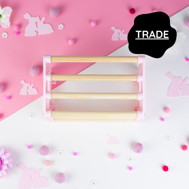 Cage mounted hay rack in pastel pink displayed on a pink background with decorative elements and &